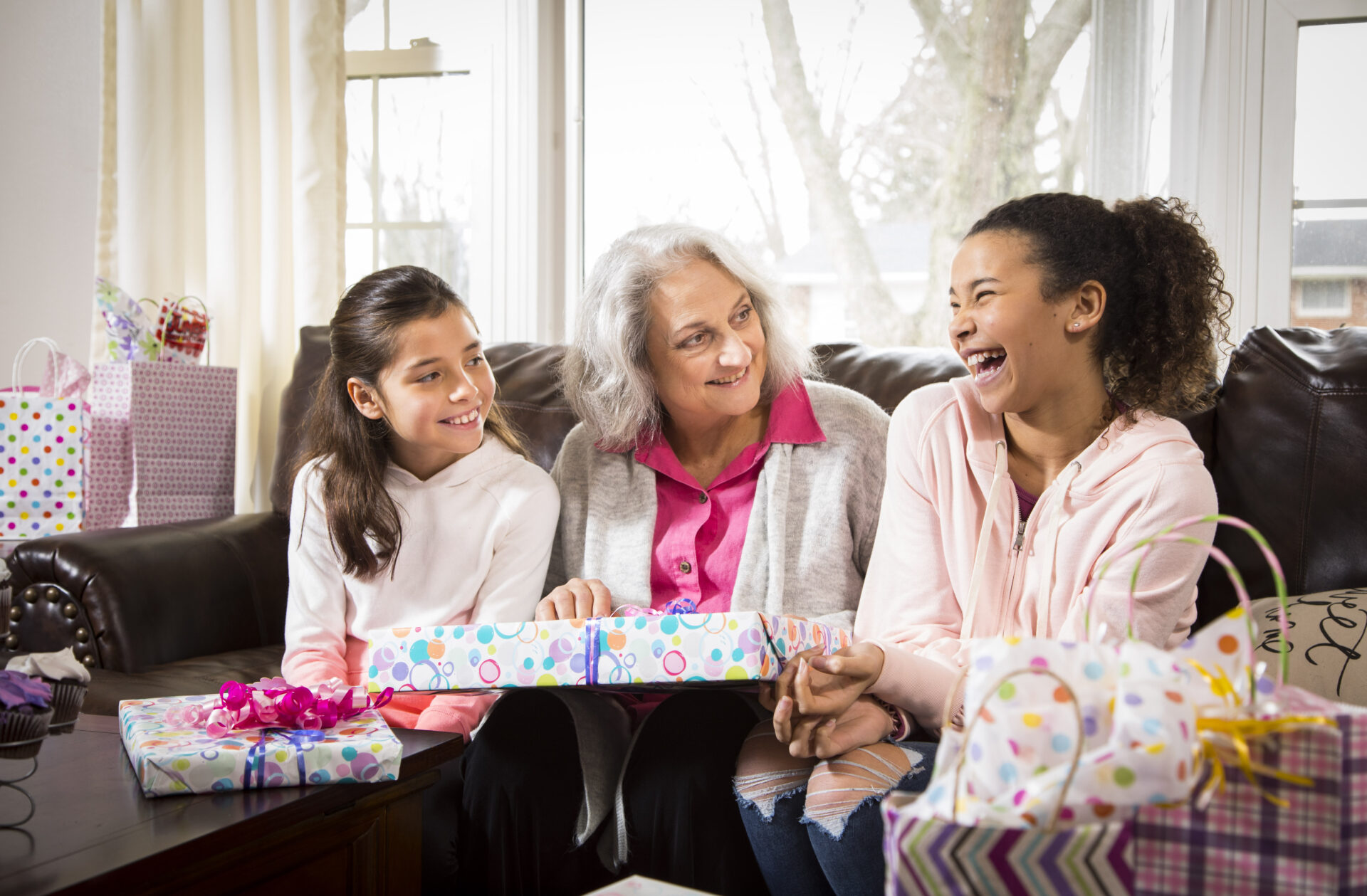 An elderly woman opening gifts with two girls
